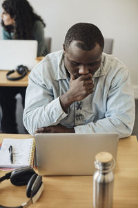 Worried male student looking at laptop while sitting in classroom