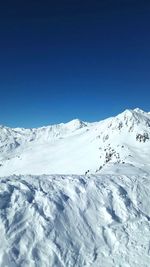 Low angle view of snowcapped mountains against clear blue sky