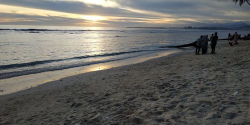 People on beach against sky during sunset