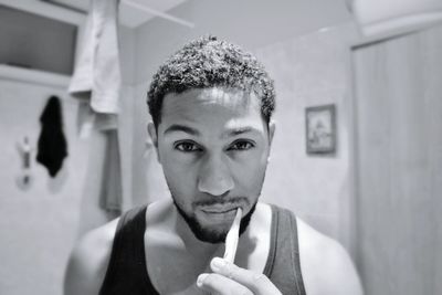 Close-up portrait of young man brushing teeth in bathroom