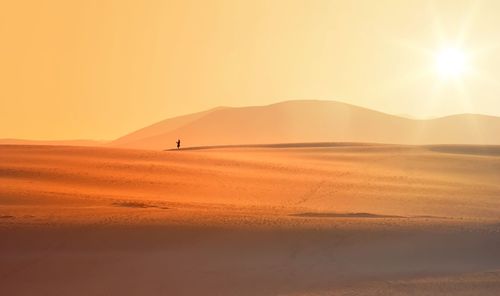 Mid distance of person standing on desert against sky during sunset