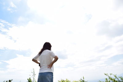 Low angle view of woman standing with hand on hip against cloudy sky