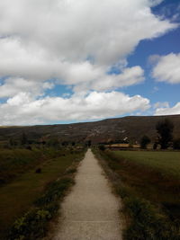 Road passing through field against cloudy sky