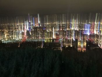 Illuminated modern buildings by river against sky at night