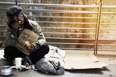 Homeless man holding sign while sitting on footpath