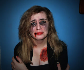 Portrait of young woman with bruises against blue wall