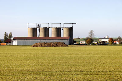 View of agricultural field and silos against clear sky