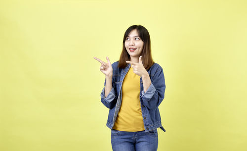 Portrait of young woman standing against yellow background