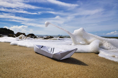 Origami paper boat on sand at beach against sky