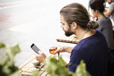 Man using mobile phone while having drink at sidewalk cafe