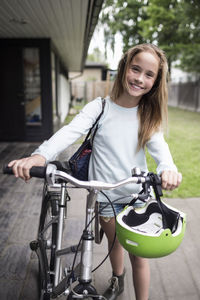 Portrait of happy girl walking with bicycle outside house