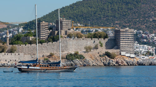 Boats in sea by townscape against mountain