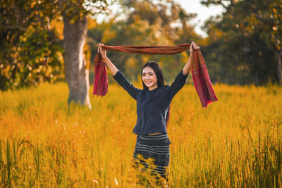 Happy young woman holding shawl while standing amidst grassy field