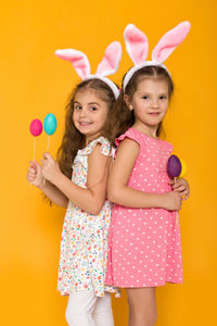 Portrait of cute girl playing with toys against yellow background