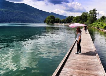 Side view of woman holding umbrella while standing on pier over lake