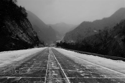 Road by mountains against sky during winter