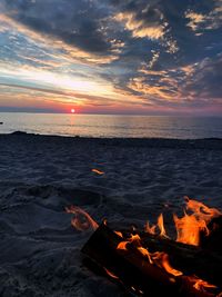 Campfire at beach against sky during sunset