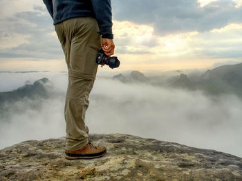 Tourist with camera in hand wearing trekking trousers and brown hiking boots. medium plan view