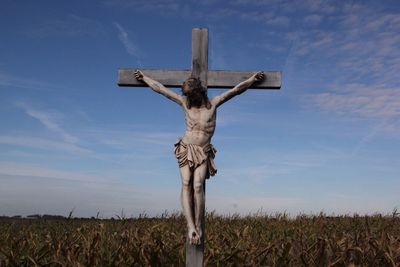 Low angle view of jesus christ statue on cross at field against sky