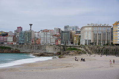 People on beach by buildings against sky in city