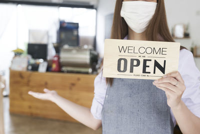 Midsection of woman holding signboard at cafe