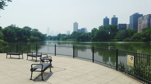 Railing by river against clear sky in city