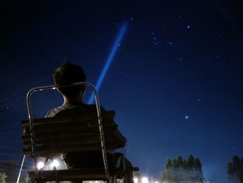 Rear view of man sitting against sky at night
