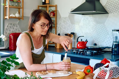 Woman making healthy breakfast or brunch, spreading peanut butter on a puffed corn cakes. 