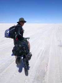 Portrait of mid adult man with bicycle standing at salar de uyuni against blue sky