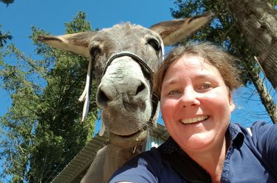 Low angle view portrait of smiling woman taking selfie with donkey