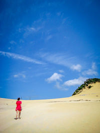 Woman walking on sand dune against sky