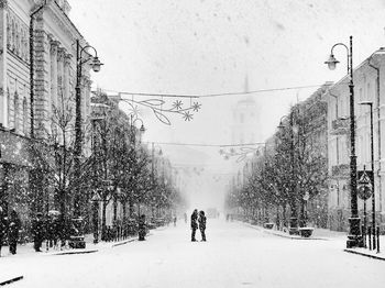 People walking on snow covered street against buildings in city