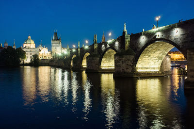 Illuminated arch bridge over river against blue sky at night