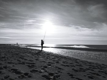 Silhouette men on beach against sky