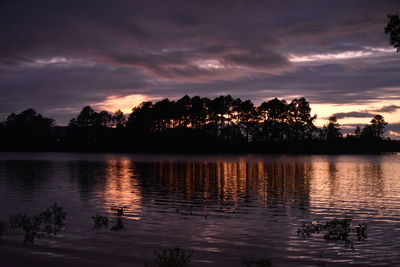 Silhouette trees by lake against sky during sunset