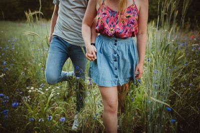 Midsection of man and woman holding hands while walking on grass