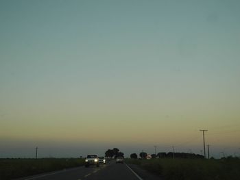 Cars on street against clear sky during sunset
