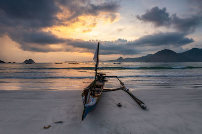 Fishing boat on beach against sky during sunset