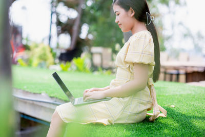 Side view of woman using mobile phone in grass