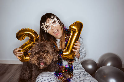 Portrait of woman wearing mask sitting with dog and balloons on floor at home