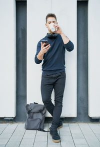 Side view of a modern man in casual clothes sitting near a white wall