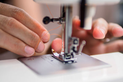 Cropped hands of woman putting thread in sewing needle at workshop