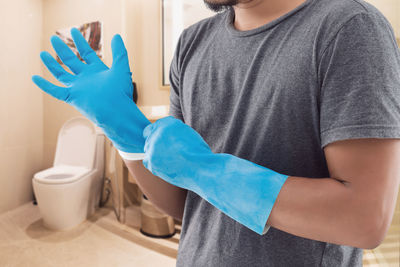 The man in a gray shirt wearing blue rubber gloves before washing the toilet.