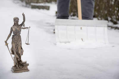Low section of person shoveling snow by lady justice statue