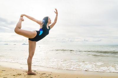 Full length of woman exercising on shore at beach against sky