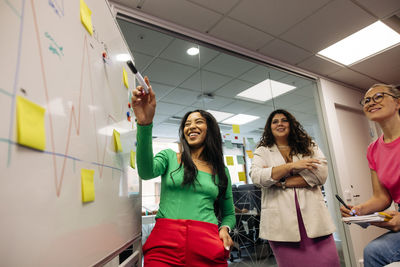 Happy female entrepreneur discussing with colleagues while doing brainstorming at office