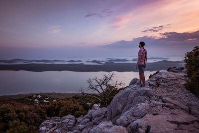 Side view of man standing on rock against sky during sunset