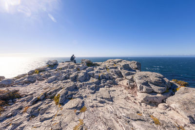 Scenic view of sea with man sitting on rock against sky