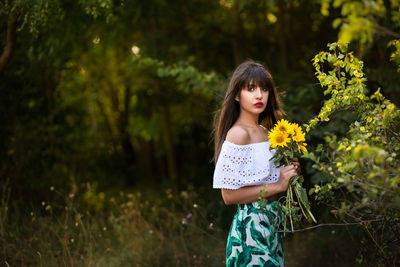 Woman holding sunflowers while standing on field