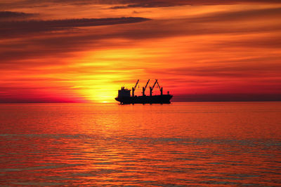 Silhouette boat in sea against orange sky